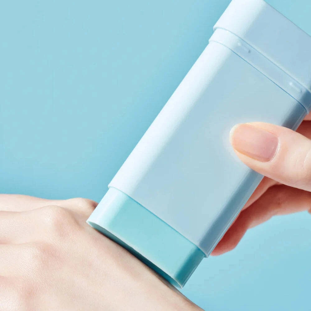 Hand applying a stick of blue deodorant on a light blue background