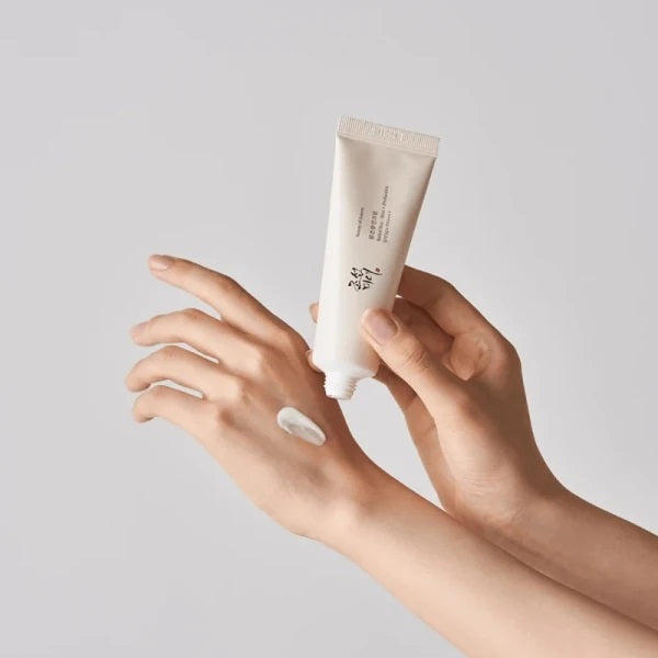 Hand applying cream from a tube on a plain background